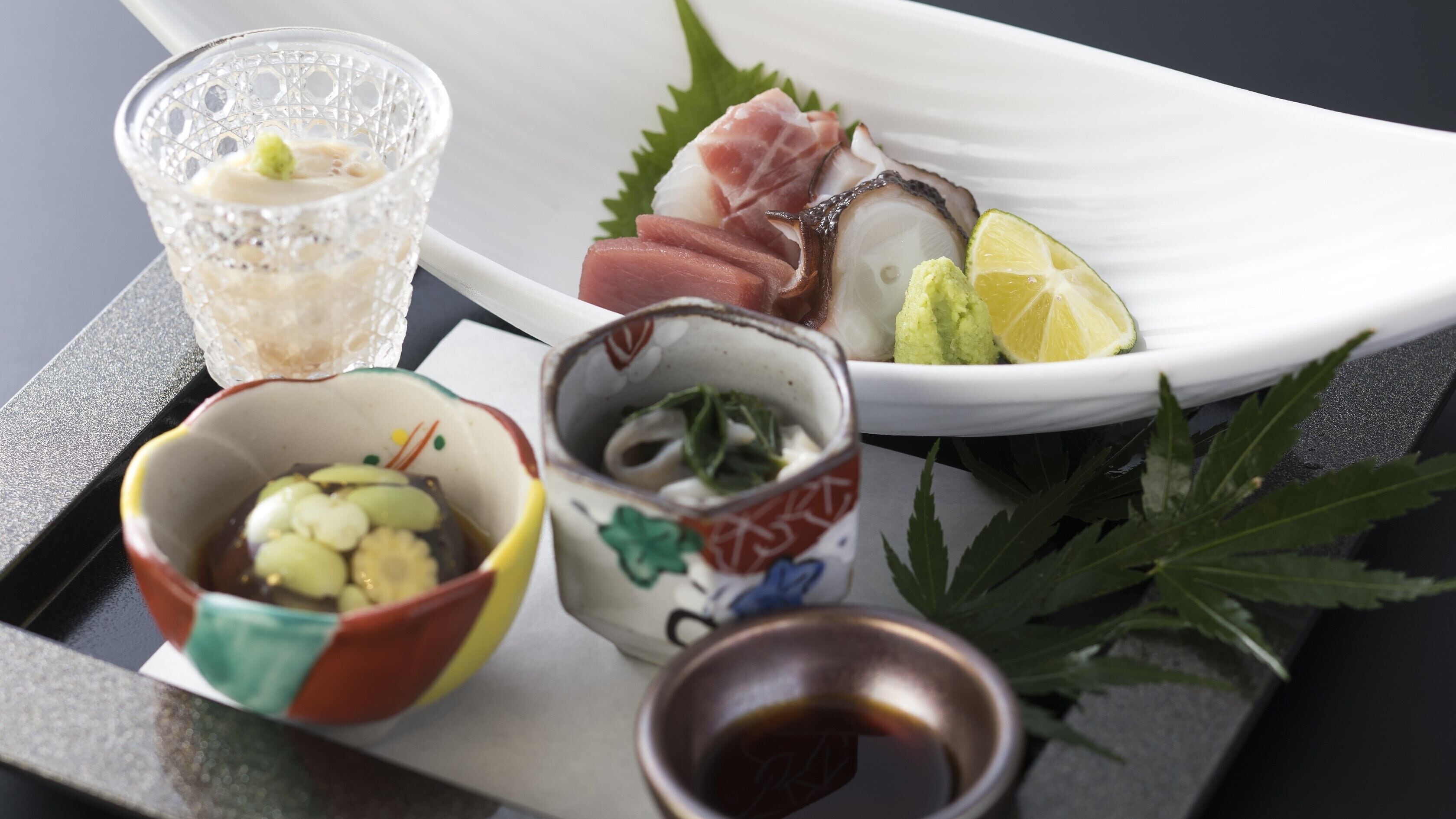 Una bandeja con sashimi, un recipiente pequeño de wasabi, una copa de sake y un tazón con salsa de soya.