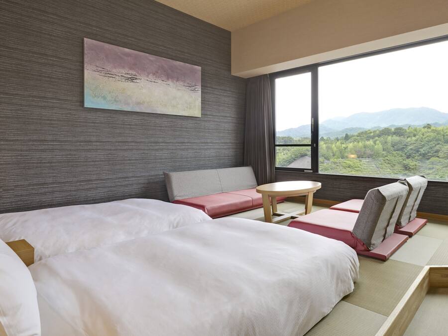 Een hotelkamer met een bed, een bank, een klein tafeltje en uitzicht op een bergachtig landschap.
