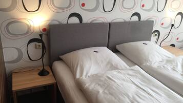A double bed with white linens, a grey headboard, and a bedside table with a lamp.