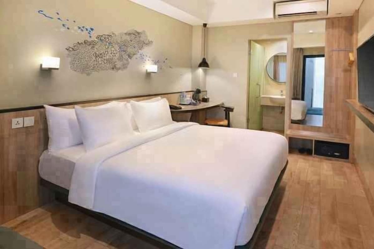 Una habitación de hotel con una cama grande, mesitas de noche, un televisor de pantalla plana y un espejo.