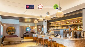 A bar area with a counter, stools, and a variety of bottles. There are signs indicating COVID-19 safety measures. - Swiss-Belinn Wahid Hasyim (Jakarta)