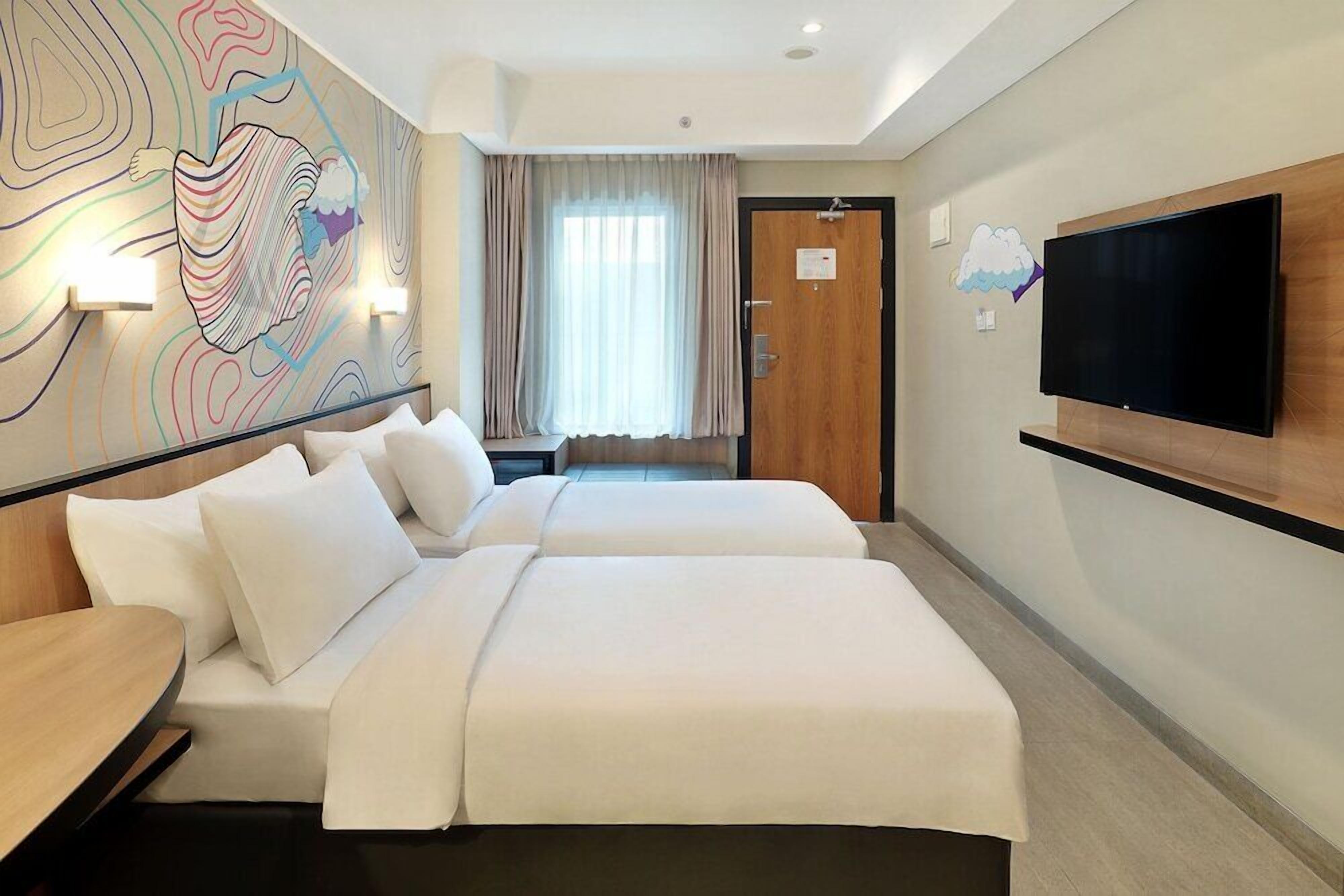 A hotel room with two beds, a flat-screen TV, a wall mural, and a window with curtains.