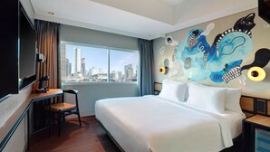 A hotel room with a large bed, a desk with a chair, a TV, and a city view. - Swiss-Belinn Wahid Hasyim (Jakarta)