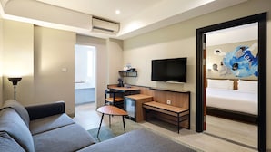A modern hotel room with a grey sofa, a small wooden desk with a TV, and a large window. - Swiss-Belinn Wahid Hasyim (Jakarta)
