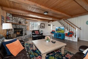 Ein gemütliches Wohnzimmer mit Kamin, Ledermöbeln, einem Holztisch und einer Treppe, die nach oben führt.