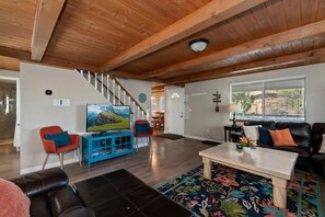 A spacious living room with a wooden ceiling, a television, a sofa, a coffee table, and a colorful rug.