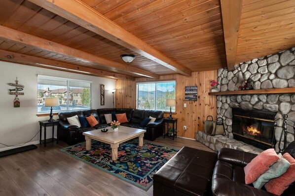 A cozy living room with a stone fireplace, wooden ceiling beams, and a leather sofa.