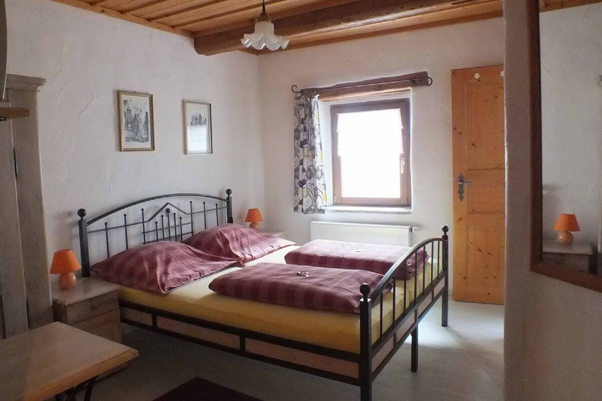 A bedroom with a bed, two bedside tables, a window with curtains, and a door.