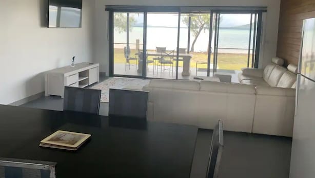 Uma sala de estar moderna com uma janela ampla que oferece uma vista panorâmica, uma área de jantar com mesa preta e um sofá branco.