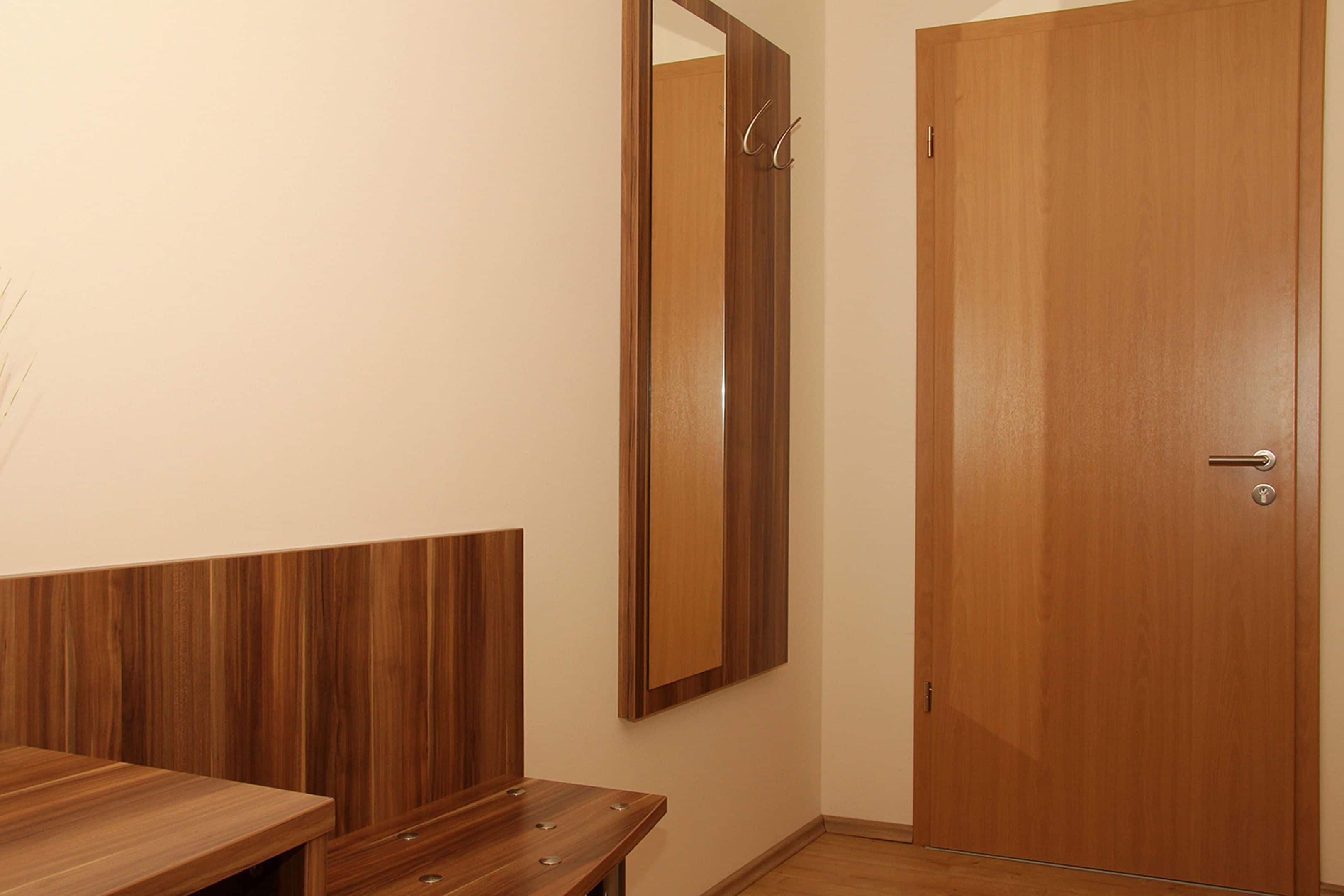 Una habitación con un banco de madera, un espejo y una puerta de madera.