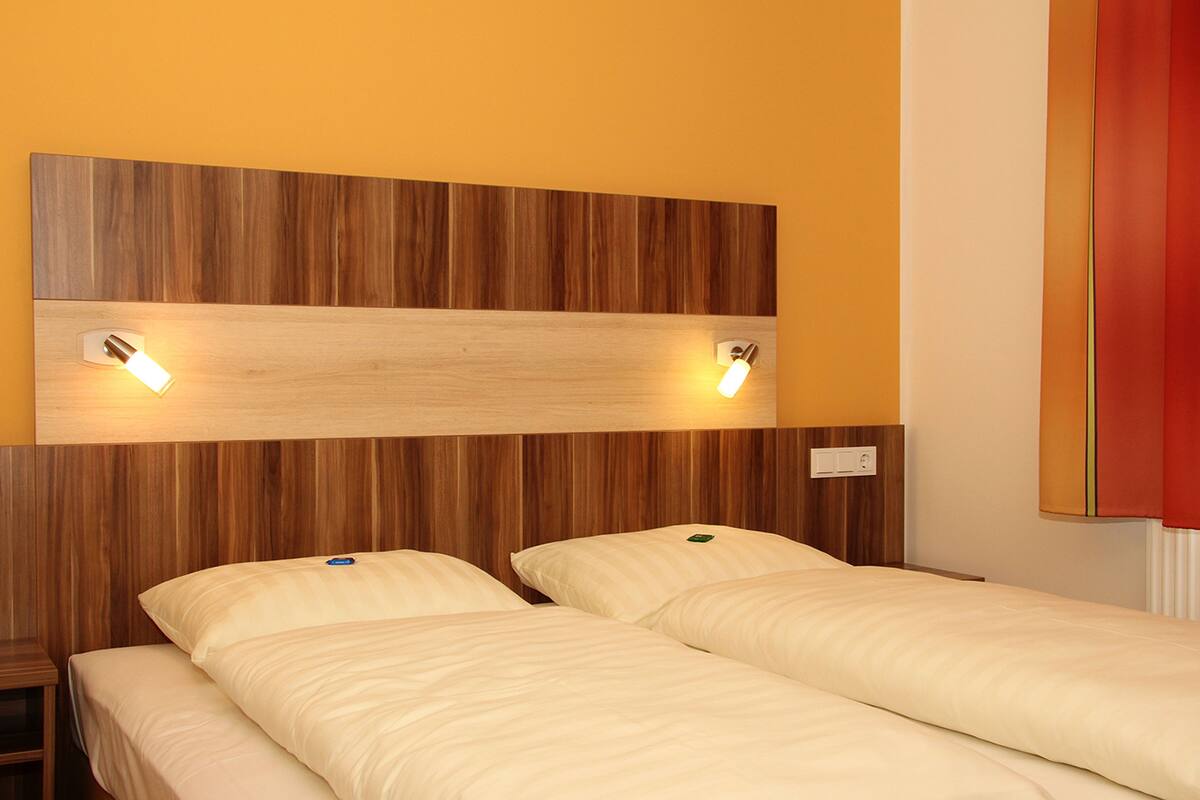 A hotel room with two single beds, wooden headboard, and bedside lamps.