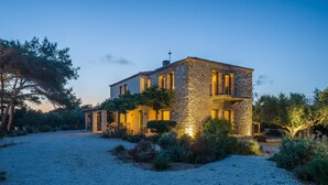 A stone house with a gravel driveway and surrounding vegetation. - Vrysomylos - Unique Villa on the beach front (Gargalianoi)