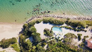 An aerial view of a resort with a swimming pool surrounded by lush greenery and a rocky shoreline. - Vrysomylos - Unique Villa on the beach front (Gargalianoi)