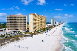 Un hotel costero con varios edificios altos, una playa de arena y un cielo azul despejado.