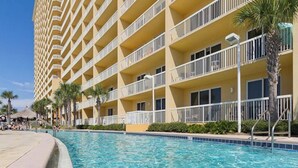 A hotel with a pool, multiple balconies, and palm trees. - Calypso 1005E - Gulf-Front Luxury, Beach Svc Included, Pier Park, Sleeps 4 (Panama City Beach)