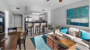 A modern living room with a dining area, kitchen, and a ceiling fan. - Calypso 1005E - Gulf-Front Luxury, Beach Svc Included, Pier Park, Sleeps 4 (Panama City Beach)