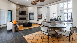 A spacious living area with a fireplace, a round dining table, and a large window providing natural light. - Fully Furnished Pool View Apartment in Tomball, TX (Tomball)