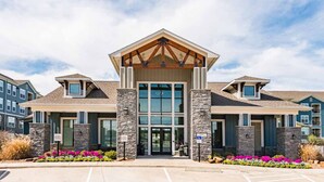A modern building with a central entrance, stone pillars, and a sloped roof. - Fully Furnished Pool View Apartment in Tomball, TX (Tomball)