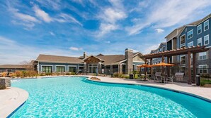 A swimming pool with a clear blue water, surrounded by buildings with balconies and a covered patio area. - Fully Furnished Pool View Apartment in Tomball, TX (Tomball)