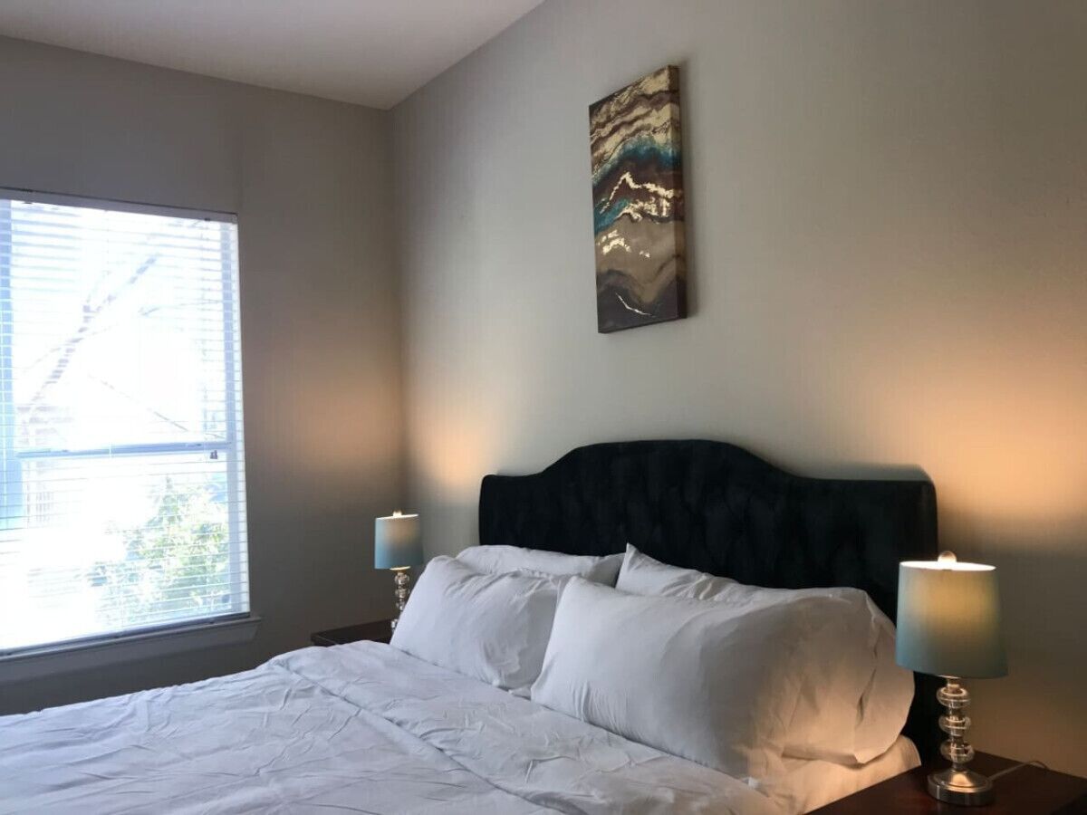 Una habitación de hotel con una cama, dos lámparas de noche, un ventanal y un cuadro en la pared.