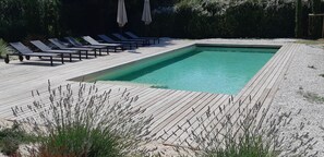 Une piscine rectangulaire dotée d’une terrasse en bois, entourée de chaises longues et de parasols.