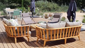 A wooden deck with a table and two wicker sofas with cushions.