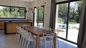 A modern kitchen with a large window, white chairs, and hanging light fixtures.