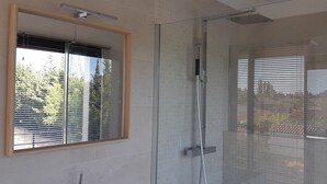 A modern bathroom with a glass shower enclosure, a large mirror, and a window with blinds.