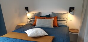 Un lit avec une couvre-lit bleue, plusieurs oreillers et une lampe de chevet.