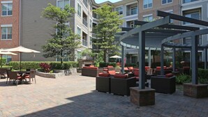 An outdoor patio area with seating and a covered section, surrounded by apartment buildings. - Spacious Furnished Apartment by NRG Stadium (Houston)
