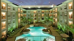 A hotel with a central swimming pool, multiple balconies, and outdoor seating areas. - Spacious Furnished Apartment by NRG Stadium (Houston)