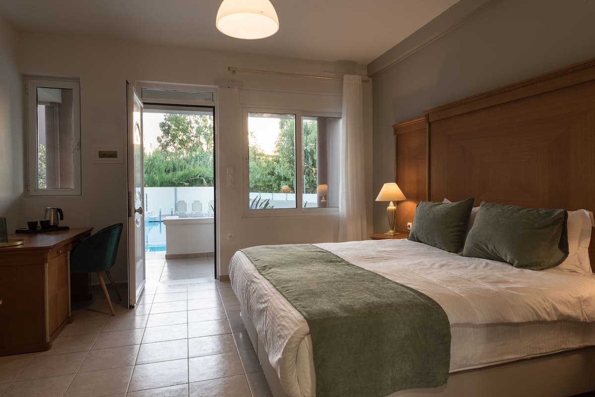A bedroom with a bed, bedside table, lamp, and a view of the outdoors through a door.
