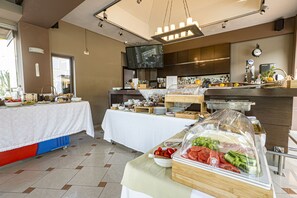 A buffet setup with various food items and a television in the background. - Okeanis 2 (Chania)