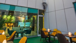 A modern coffee shop with a neon sign, outdoor seating, and a green carpeted area. - Al Malqa Elite Hotel (Riyadh)