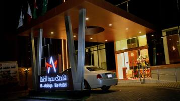 A hotel entrance with a modern design, featuring a prominent illuminated sign and a car parked in front.