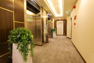 A hotel corridor with elevators, potted plants, and a carpeted floor.