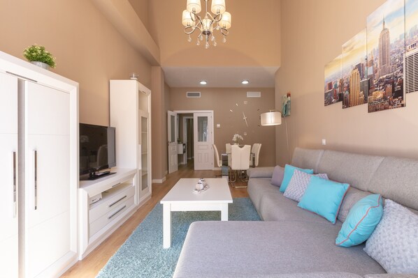 Una sala moderna con un sofá, televisor, mueble blanco y una pintura de un paisaje urbano.