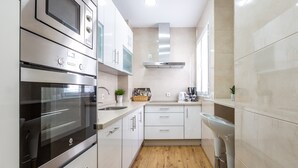 Une cuisine moderne dotée d’appareils électroménagers en acier inoxydable, de meubles blancs, d’un plancher en bois et d’un tabouret de bar.