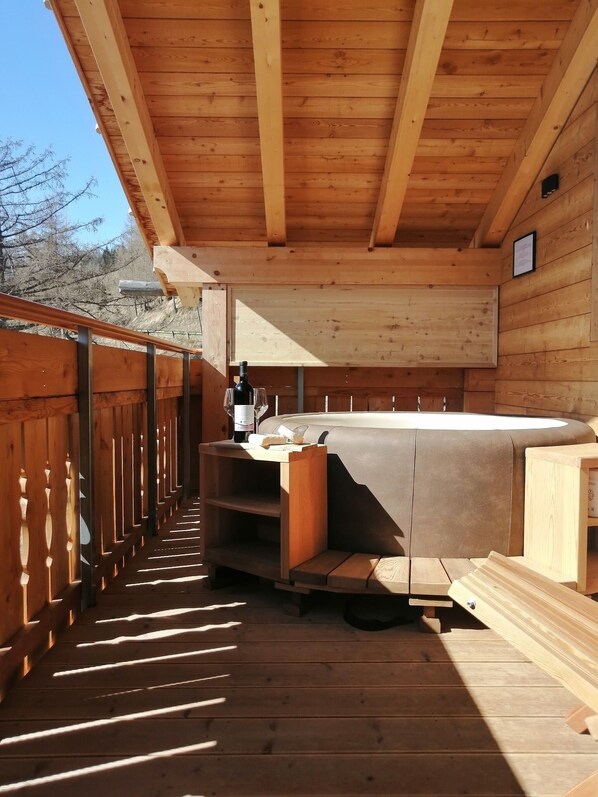 Une terrasse en bois avec un jacuzzi, des rampes en bois et une bouteille de vin.