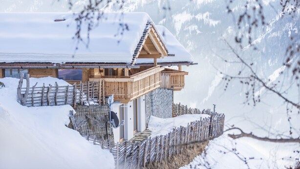 A wooden chalet with a balcony, surrounded by snow and a wooden fence.