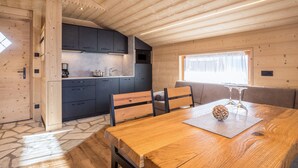 A wooden interior with a dining table, chairs, a kitchen area, and a window.