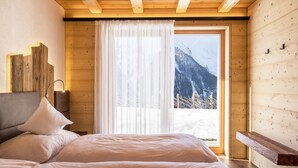 A bedroom with a bed, a window with curtains, wooden walls, and a view of mountains.