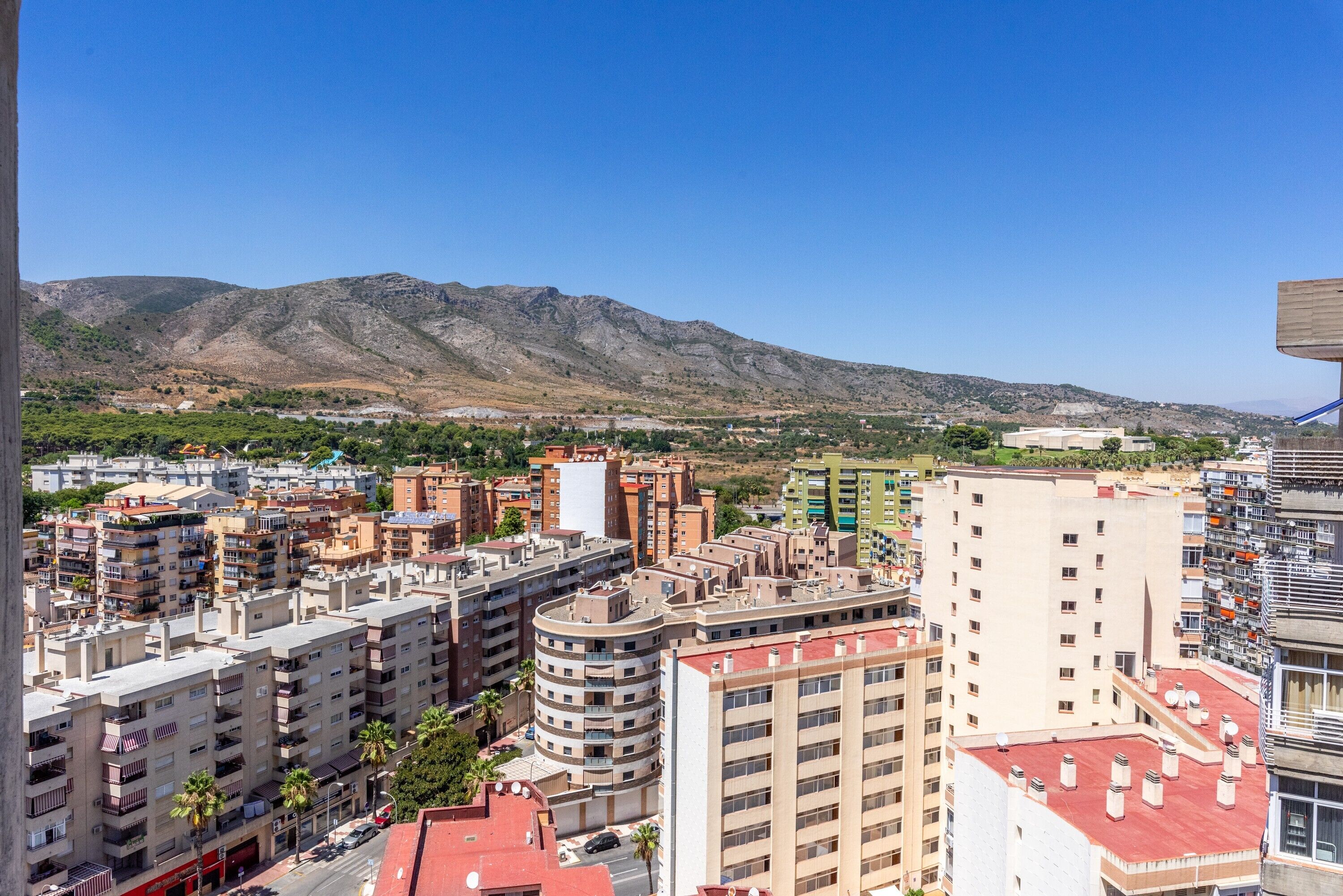 A cityscape with high-rise buildings, a mountain in the background, and a clear sky.