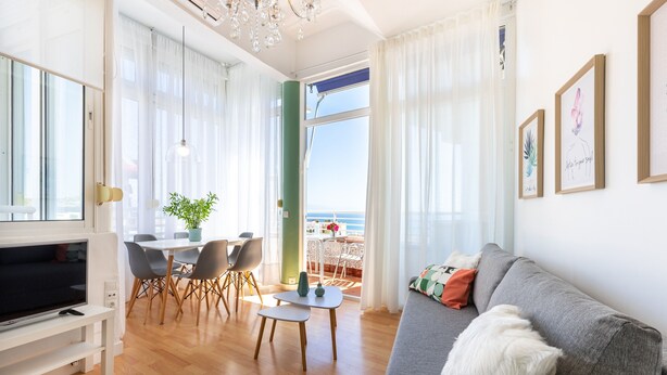 Una sala de estar moderna con televisor, sofá, mesa de comedor, sillas y vista al mar.