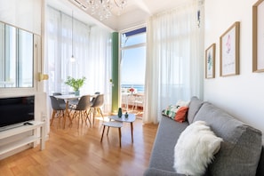 Un soggiorno moderno con televisore, divano, tavolo da pranzo, sedie e vista sul mare.
