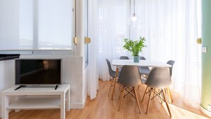Un área de comedor moderna con un televisor sobre un mueble bajo, una mesa de comedor con sillas y una planta en maceta.