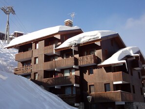 A multi-story wooden building with balconies covered in snow, set against a clear sky.