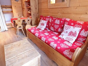 A wooden cabin interior with a sofa bed, wooden chairs, and a small table.
