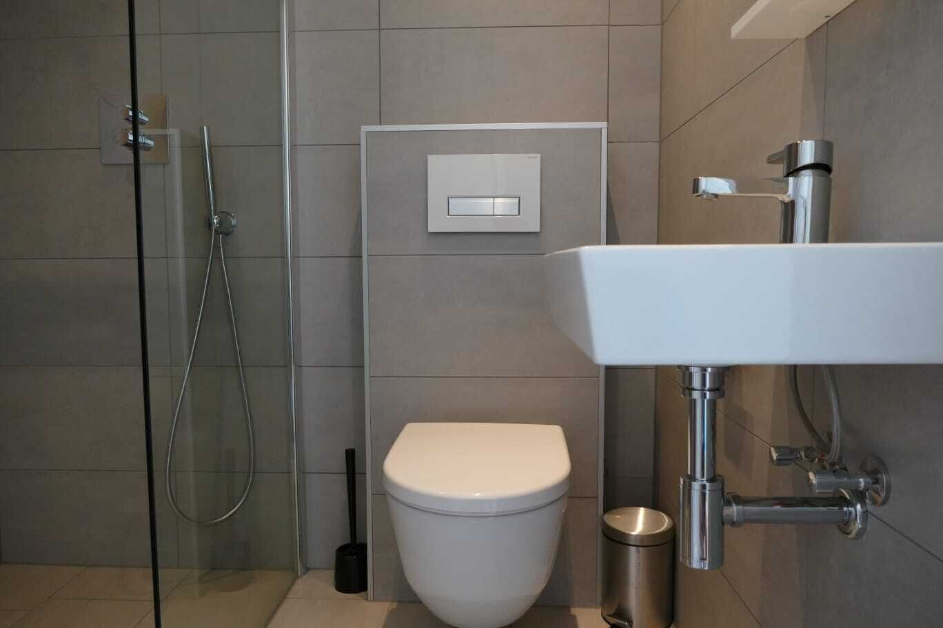 Et moderne badeværelse med en glasbrusekabine, toilet og et vægmonteret håndvask.