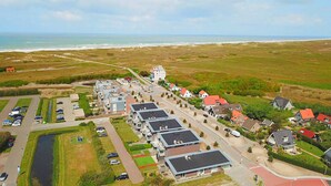 Vista aérea de una zona residencial costera con casas, un estacionamiento y una playa al fondo.
